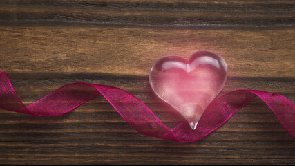A glowing glass heart and a bright ribbon on a wooden background. The concept of Valentine's Day.