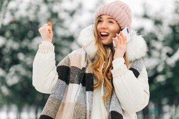 Happy excited beautiful woman in winter clothes talking on a mobile phone and celebrating victory...