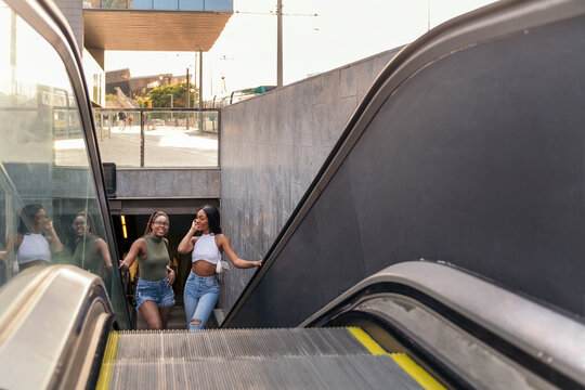 two black girls going up the escalator at subway - Powered by Adobe