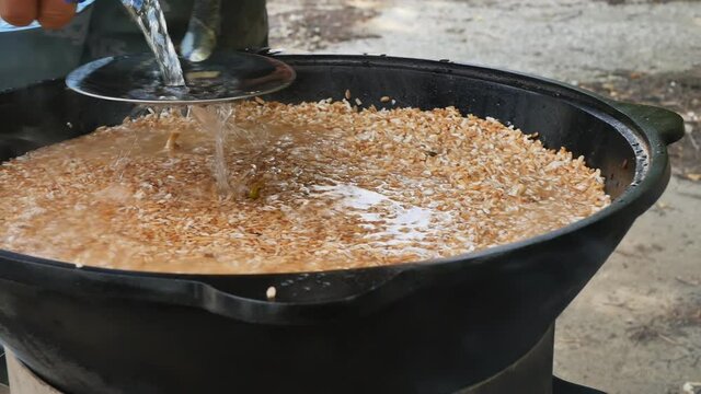 the cook prepares the Uzbek pilaf in the open air in a cast iron cauldron. Pour water into the rice through a slotted spoon. Slow motion, close up