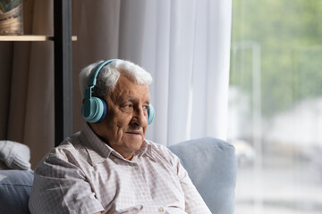 Head shot relaxed smiling old mature retired 80s man wearing wireless headphones, listening favorite audio tracks, enjoying pop music spending carefree leisure weekend hobby time alone at home.