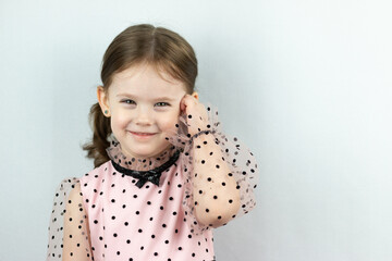 Smiling little girl with two ponytails in a dress with polka dots on a white background touches her...