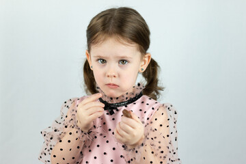 Smiling little girl with two ponytails in a dress with polka dots on a white background offers a chocolate candy. Studio photo