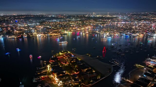 Christmas boat festival in Newport beach. Colorful and brightly illuminated boats fast moving in bay at night 4K USA. Cinematic aerial hyper lapse of people celebrating winter season holidays boat
