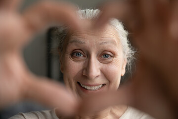 Close up head shot happy beautiful middle aged old retired woman making heart symbol, expressing sincere love and support. Cheerful kind mature grandmother volunteer showing candid feelings and care.