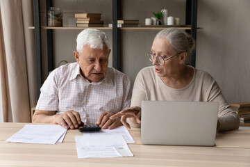 Concentrated middle aged mature family couple calculating domestic expenditures or taxes, managing...