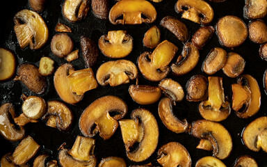 Fototapeta premium Pan-fried Champignon mushrooms on a frying pan background. Top view dark food pattern.