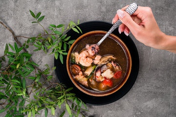 Hand holding a spoon with a shrimp and fish, Seafood Diet soup