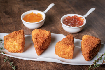 Fried Camembert cheese in portions presented on a tray alongside two flavored jams.