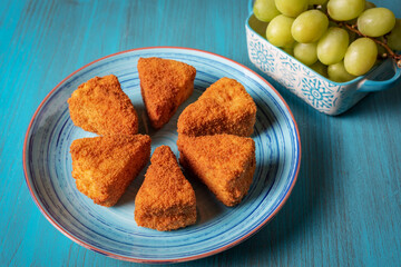 Camembert cheese fried in portions and presented with a bunch of grapes.