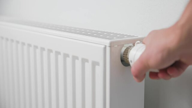 Hand adjusting temperature on heating radiator thermostat, Turning heat radiator knob to control heat in home