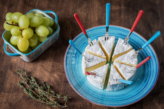 Camembert cheese in portions next to a bunch of grapes.