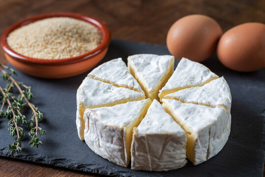 Camembert cheese cut into portions along with breadcrumbs and eggs, ingredients to cook it fried.