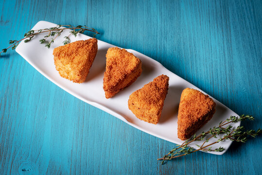 Fried Camembert cheese in portions presented on a tray and on a light blue wooden table.
