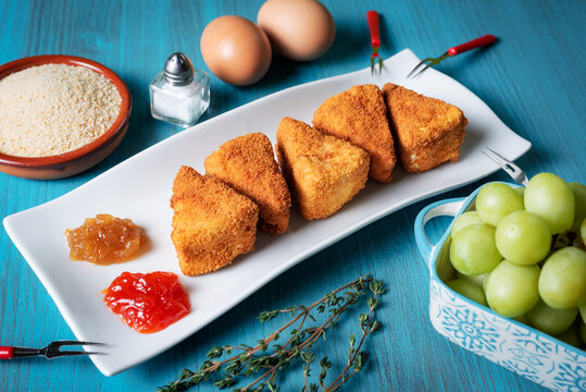 Fried Camembert cheese in portions with breadcrumbs, eggs,marmalade and grapes.