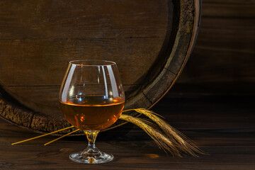 Glass decanter with whiskey, brandy on a vintage background of a rustic oaken barrel. Alcoholic beverage. Still life in the old style