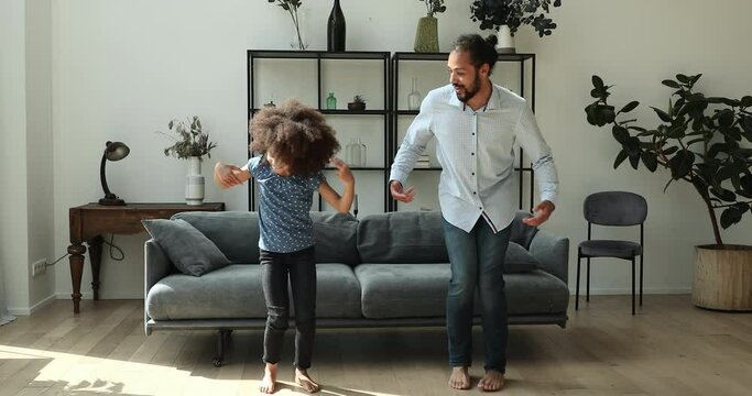 Full length of African father and cute lively curly haired daughter perform famous in social media dance, funny moving, dancing barefoot together in cozy living room. Family leisure and hobby concept