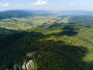 Aerial view of mountain hills covered with dense green lush woods on bright summer day