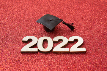 Graduat hat with wooden number 2022 on red glittering background. Education, leaning, class 2022...
