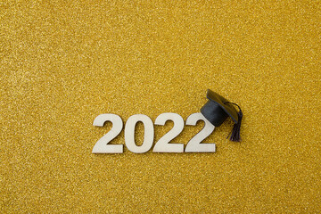 Graduation 2022 wooden number 2022 wearing graduate hat on golden glittering background top view