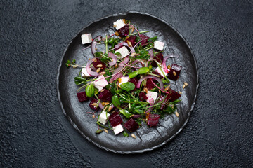 Salad of microgrin, beetroot and cheese with fresh onions and seeds on a plate on a black background. top view