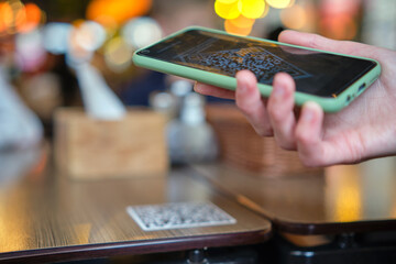 Closeup of guest hand ordering meal in restaurant while scanning qr code with mobile phone for online menu