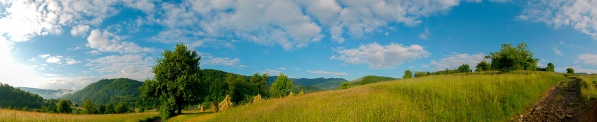 Fototapeta premium Panorama with piles of hay in the mountains. Morning with fog in the valley.