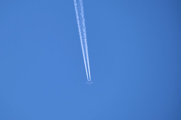 Distant passenger jet plane flying on high altitude on clear blue sky leaving white smoke trace of contrail behind. Air transportation concept