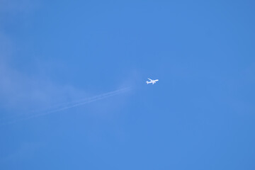 Distant passenger jet plane flying on high altitude on clear blue sky leaving white smoke trace of contrail behind. Air transportation concept