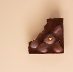 a broken or bitten piece of chocolate with whole hazelnuts. ecru color background.