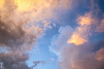 Dramatic moody sunset landscape with puffy clouds lit by yellow setting sun and blue sky