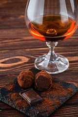 Glass of brandy and a chocolate truffles with chocolate on an old wooden table