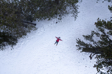 Drone aerial of woman wearing warm clothing lie down at snow in winter. Troodos cyprus
