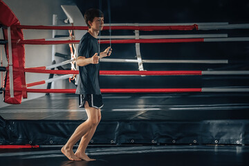 A young guy of an athletic physique is doing a warm-up in the gym, jumping rope. The concept of a healthy, active, sporty life for a teenager.