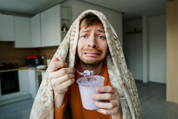 Portrait of heartbroken young man eating ice cream from bucket. Sad guy crying over breakup.