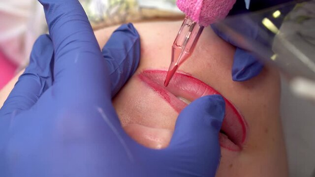 Close up process of applying permanent makeup tattoo of red on lips woman in beautician salon