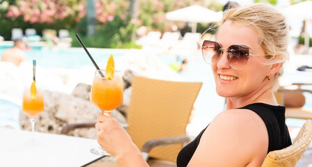 Bright orange cocktail stands on edge of pool