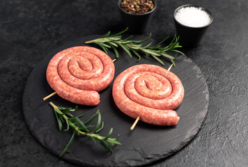 raw sausages in the form of a spiral on skewers on a stone background
