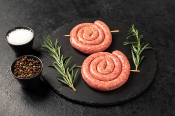 raw sausages in the form of a spiral on skewers on a stone background