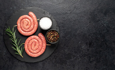 raw sausages in the form of a spiral on skewers on a stone background with copy space for your text