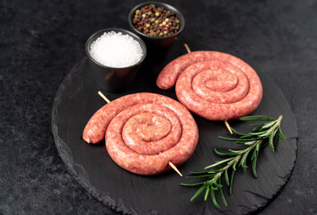 raw sausages in the form of a spiral on skewers on a stone background
