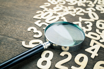 Closeup magnifying glass in scattered numbers on wood background, calculation, mathematics concept