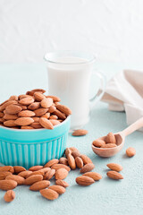 Peeled almonds in a bowl and almond milk in a glass on a light background. Alternative nutrition, source of vitamins. Vertical view
