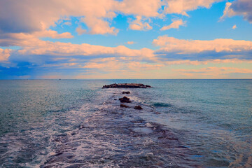 A pier made of stones, a pier leading into the sea. Beautiful sunset sky with clouds.