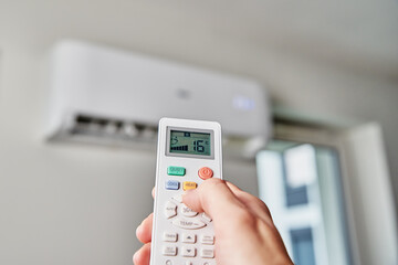 Hand adjusting temperature on air conditioner with remote control, Working air conditioner for...