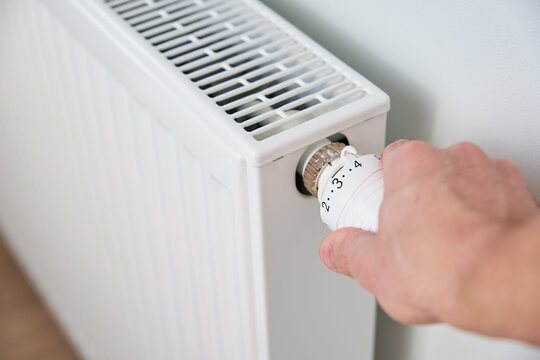 Hand adjusting temperature on heating radiator thermostat, Turning heat radiator knob to control heat in home