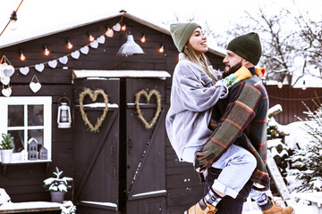 Fototapeta na wymiar couple of young woman and man having fun in courtyard of decorated suburban house in winter, concept of Christmas and New Year vacation on farm, family love and support, Valentines Day celebration