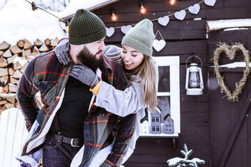 couple of young woman and man having fun in courtyard of decorated suburban house in winter, concept of Christmas and New Year vacation on farm, family love and support, Valentines Day celebration