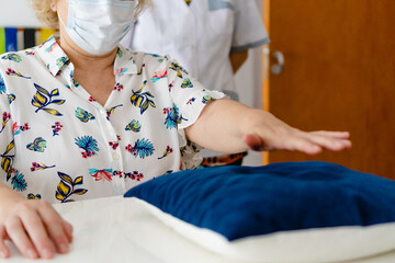elderly woman rehabilitating tendinitis in shoulder pushing a pillow accompanied by occupational therapist, kinesiologist