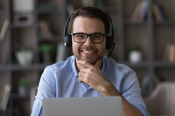 Head shot portrait smiling man call center operator in glasses looking at camera, using laptop,...